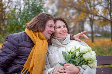 Midlife couple enjoying a romantic moment in autumn park, surrounded by colorful leaves, holding roses, sharing laughter and warmth, celebrating love and connection