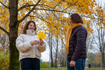 Midlife couple enjoying autumn day in park, surrounded by vibrant yellow leaves, sharing joyful moments and laughter, celebrating the beauty of fall together