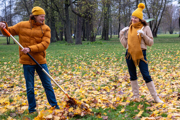 Midlife couple enjoying autumn outdoors, raking colorful leaves in a park, surrounded by vibrant fall foliage, creating a cozy seasonal atmosphere with copy space
