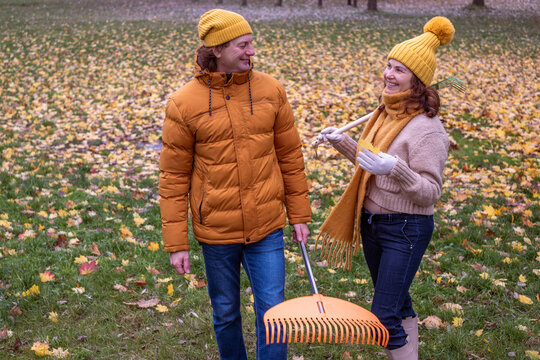 Midlife couple enjoying autumn day, raking colorful leaves in a park, wearing cozy sweaters and hats, creating a joyful atmosphere of seasonal activities and togetherness