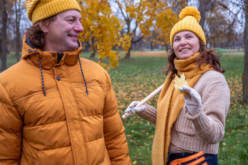 Midlife couple enjoying autumn outdoors, raking colorful leaves in a park, wearing cozy sweaters and hats, capturing the essence of fall together with joy and laughter
