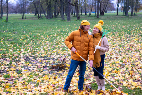 Midlife couple enjoying autumn day together, raking colorful leaves in a park, surrounded by vibrant foliage, creating a cozy fall atmosphere with copy space