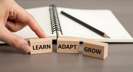 Hand arranging wooden blocks with words learn adapt grow next to notebook