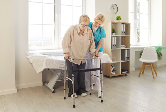 Woman caregiver helping mature woman to walk with help of walkers, supporting during therapy, teaching and giving advice, posing in rehab. Rehabilitation and disabled people concept