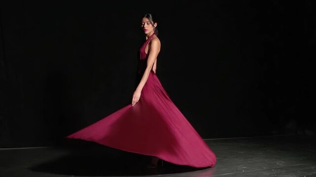A woman poses in a flowing maroon dress with a high slit against a dark backdrop