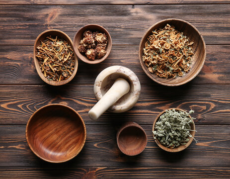 Overhead shot of wooden bowls with herbs and spices and a mortar and pestle on wooden surface