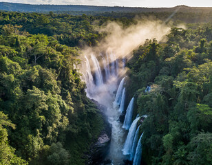 Aerial view of a large waterfall cascading through a dense green forest on a sunny day landscape