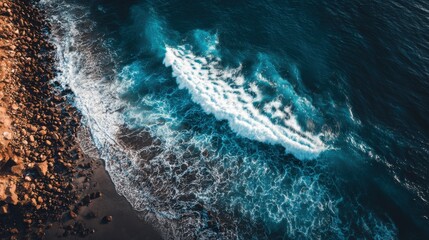 Stunning Aerial View of Ocean Waves Crashing on Rocky Shoreline Surrounded by Blue Waters and Sandy Beach Under Bright Sky