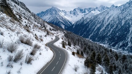 Obraz premium A drone shot of a winding mountain road surrounded by snow-capped peaks. 