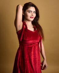 High-quality studio portrait of an elegant woman wearing a red velvet dress, posing confidently with her hand in hair and holding a rose against a yellow backdrop. Ideal for fashion, beauty, lifestyle