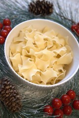 Uncooked cube-shaped pasta in small bowl decorated with Christmas ornaments. Festive holiday meal concept.