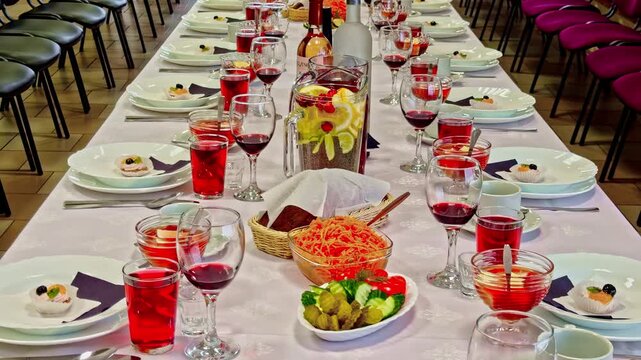 Long banquet table set for a large dinner with food, drinks, and rows of chairs.