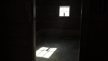 Dark horse stall interior, rustic wooden barn room with light streaming through a small window, dramatic shadow on the floor. strong contrast between darkness and sunlight - Powered by Adobe