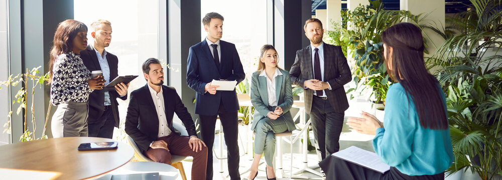Businesswoman conducting a work conference or meeting for a team of colleagues in an office. The group of people is engaged in productive conversation, showing effective teamwork and collaboration.