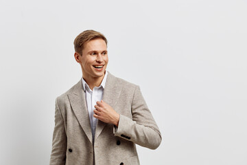 Smiling young man in stylish beige blazer and white shirt showing confident expression on plain...