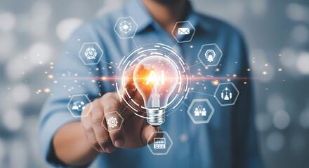A person's hand touches a glowing lightbulb with digital icons representing innovation and technology, showcasing creative ideas and solutions.