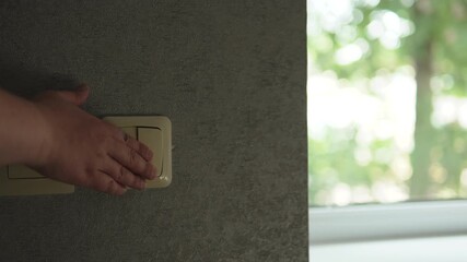 Hand presses switch and roller blinds on windows lower, darkening room. Privacy, security, and comfort in residential buildings.