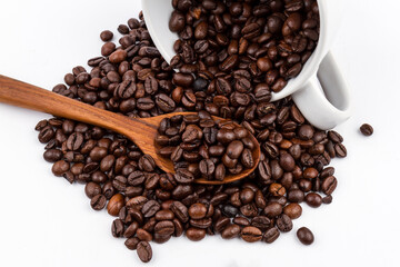 Roasted coffee beans spilling from a white ceramic cup, with a wooden spoon holding a fresh scoop of beans.