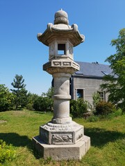 Fototapeta premium Stone lantern structure stands tall in a lush garden, surrounded by greenery and blue sky, showcasing traditional design and serene outdoor ambiance
