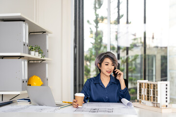 Professional civil engineer in construction site office. Talking on phone call working on shop drawings of post tension slab plan on desk.