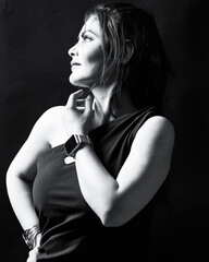 Black and white fine-art portrait of a woman in a one-shoulder dress, wearing wrist accessories and looking upward under studio lighting. Perfect for concepts of confidence, introspection, fashion