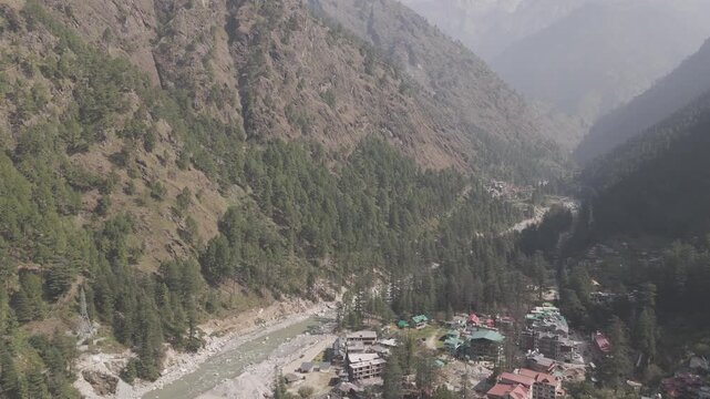 Aerial view of Parvati Valley near Chalal village showing Parvati River, scattered village houses, rocky Himalayan mountains, and dense pine&ndash;deodar forests under a cloudy autumn sky.