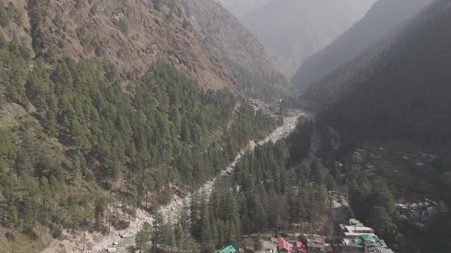 Aerial view of Parvati Valley near Chalal village showing Parvati River, scattered village houses, rocky Himalayan mountains, and dense pine&ndash;deodar forests under a cloudy autumn sky.