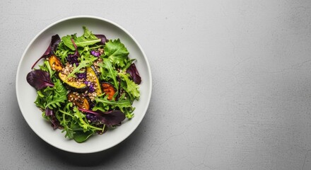 Fresh green salad with colorful leaves and fruits in a white oval bowl. Fresh salad with roasted plums, arugula, spinach and sesame seeds on a gray background