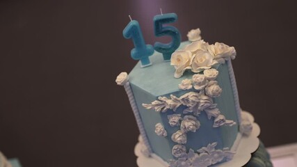 Slow reveal showcases a hexagonal blue fondant cake adorned with cascading white flowers and number candles “15,” highlighting artistic detail and celebration mood for a milestone birthday.