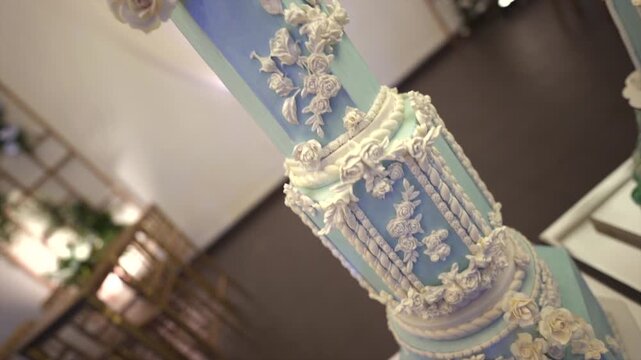 An upward camera motion reveals a tall tiered wedding cake in pastel blue with white floral and scrollwork icing, showcasing intricate craftsmanship and elegance in a formal banquet setting.