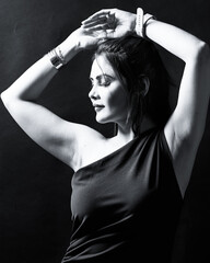 Studio portrait of a woman in a black dress captured in graceful motion with soft lighting. The monochrome tone emphasizes elegance, strength, and timeless beauty.
