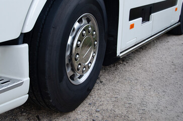 A close-up side view of a large white truck's wheel and tire, with a clean, metallic hubcap. The truck is parked on a dirt road.