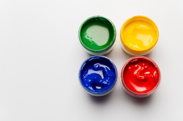 Gouache on a white background. A set of gouache paints in uncapped bottles. Children's art project. An artist's palette of different paints, close-up. Top view with empty space