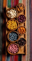 Overhead view of a wooden tray holding seven small wooden bowls, each filled with a different variety of colorful, possibly candied, nuts and beans.