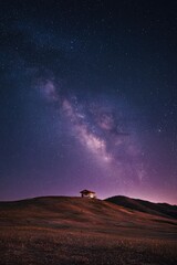 Solitary structure atop a gently sloping hill under a vibrant night sky, showcasing a brilliant Milky Way galaxy with countless stars