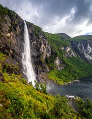 Obraz premium A tall waterfall cascades down a rocky cliff surrounded by lush green foliage