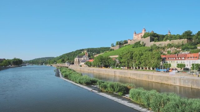 Wide-angle landscape of the Main river flowing past the Marienberg Fortress perched on a hill, overlooking the historic city and vineyards. Sunny day scene of German travel and architecture.