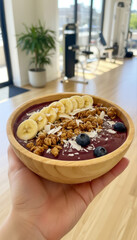 Acai bowl with banana, granola, and blueberry held in hand at the gym, showcasing a healthy and delicious postworkout meal option