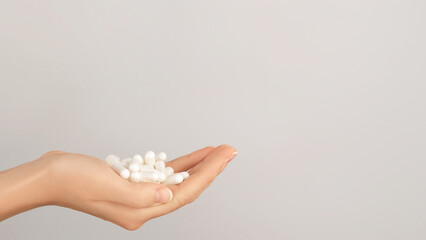 Hand holding a pile of white capsules on a neutral background, symbolizing medicine, supplements,...