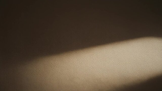 A minimalist shot of a textured wall surface with a diagonal beam of natural light creating a strong contrast between shadow and illumination.