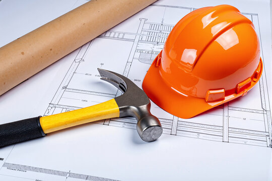 Construction project concept with an orange hard hat, hammer, and rolled blueprints resting on architectural plans, representing building, safety, and engineering