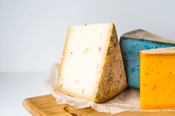 Unusual taste and quality of fresh farm products. Pieces of different fresh, aged, natural farm cheese in parchment paper on a wooden board.