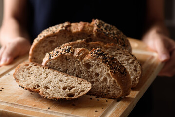 Dark rye sourdough bread topped with sesame seeds, a healthy vegetarian food, held in a woman's hand.