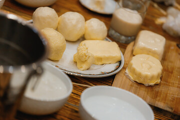 A rustic kitchen scene with various dairy products: round dough balls, blocks of butter, and a glass of creamy beverage on a wooden table. White bowls and kitchen utensils add to the homely, artisanal