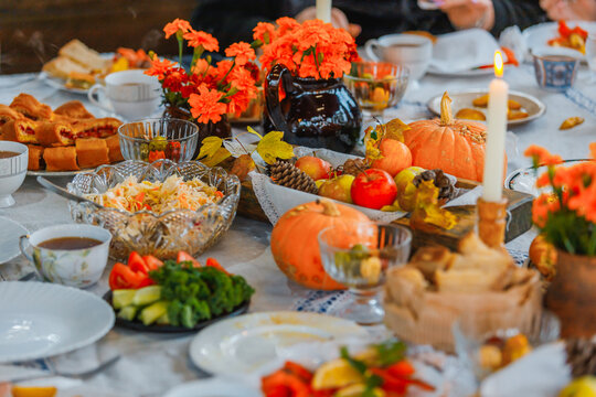 A festive autumn table setting with pumpkins, apples, pinecones, vibrant orange flowers, and a lit candle. Crystal bowls, teacups, and plates of fresh salads and pastries create a cozy harvest-time