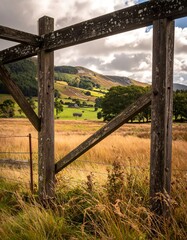 A rustic wooden fence frames a scenic valley view under a cloudy sky
