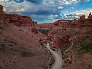 Aerial view of Charyn Canyon with red rock walls, winding valley road and dramatic evening clouds....