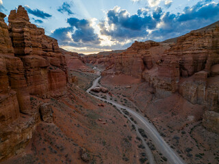 Aerial view of Charyn Canyon at sunset with red rock cliffs, a winding road and a dramatic cloudy sky. Kazakhstan desert landscape