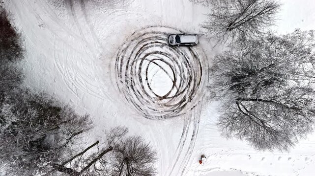 A vehicle creates perfect concentric circles in fresh snow, blending automotive skill with winter landscape artistry in a stunning aerial view.