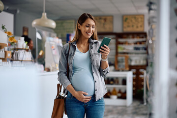 Happy expecting woman using app on cell phone while shopping in a drugstore.